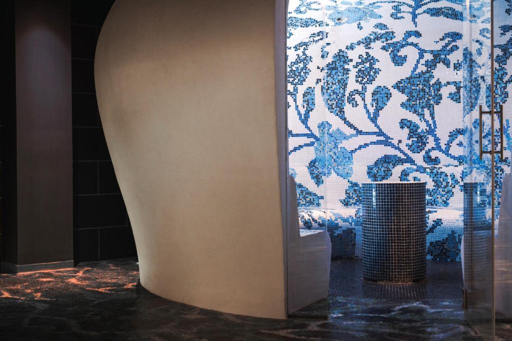 Mūsdienīgs interjers ar gludu, pelēku sienu un zilu mozaīkas apdari, kas veido dekoratīvu elementu. Izsmalcināta atmosfēra un eleganta dizaina detaļas.