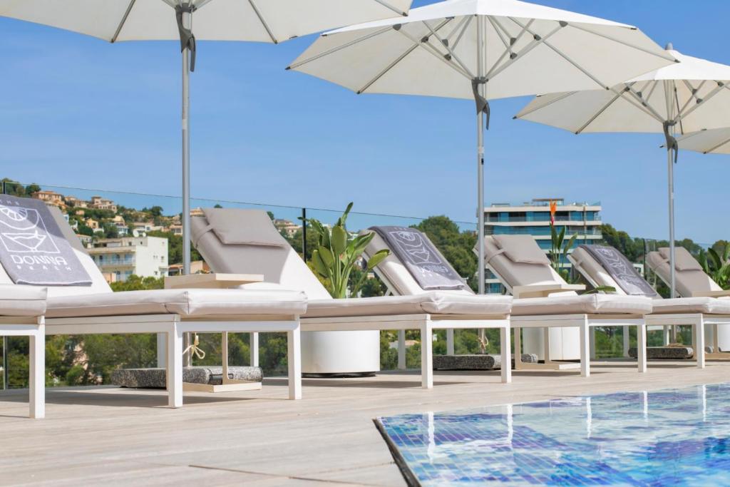 Baseina atpūtas zona ar sauļošanās krēsliem un baltiem saulessargiem, skats uz zaļo dabu un viesnīcas kompleksu. Ideāla vieta relaksācijai un atpūtai.