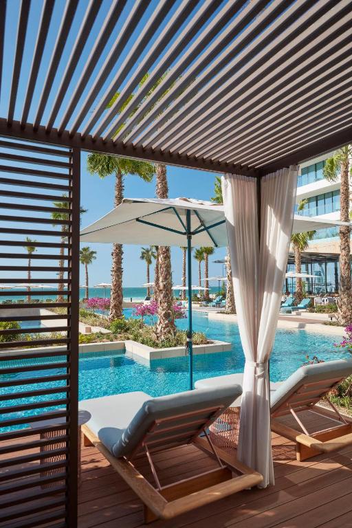 Mūsdienīgs atpūtas zona ar sauļošanās krēsliem un baseinu, ko ieskauj palmas un ziedi, radot relaksējošu atmosfēru. Ideāla vieta atpūtai pie jūras.
