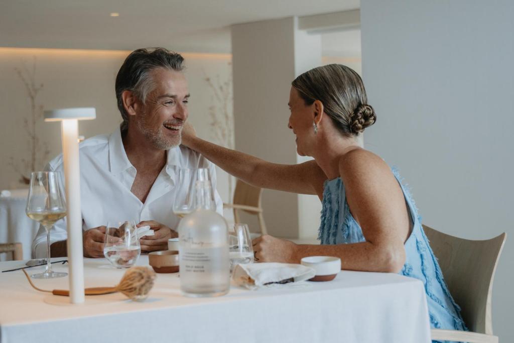 Pāris bauda romantisku vakariņu pieredzi elegantā restorānā, sēžot pie galda ar vīnu un gaismas avotu. Atmosfēra ir silta un intīma.