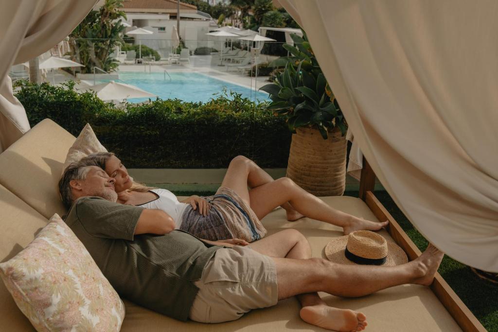 Romantisks brīdis pāra atpūtā, guļot zem balta auduma, ar baseinu fonā. Ideāla vide relaksācijai un mīlestības baudīšanai.