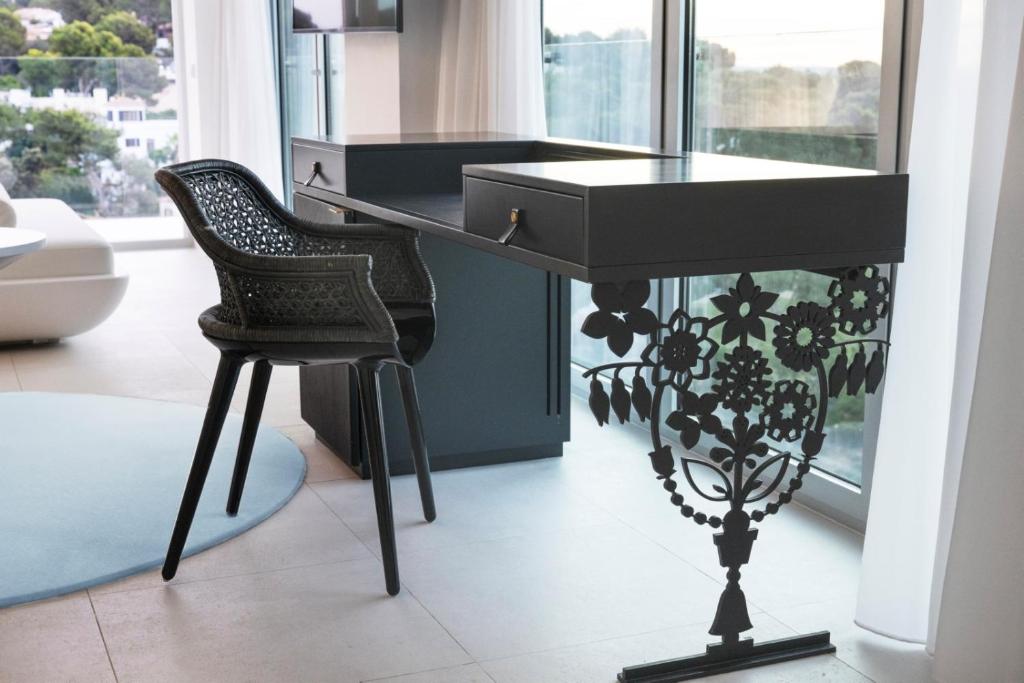 Mūsdienīga rakstāmgalds ar dekoratīvu ziedu motīvu un stilīgu krēslu, izvietots telpā ar lieliem logiem un skatu uz dabu.