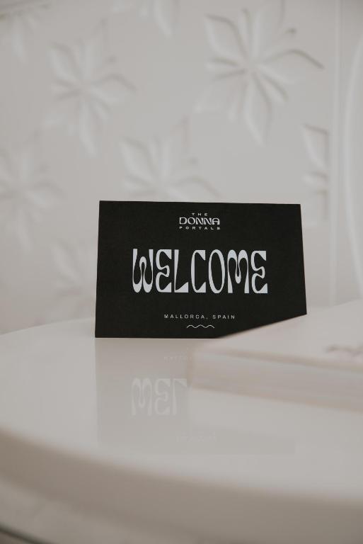 Sveicināti! Melna kartīte ar baltu uzrakstu "WELCOME" un "MALLORCA, SPAIN", novietota uz balta galda.