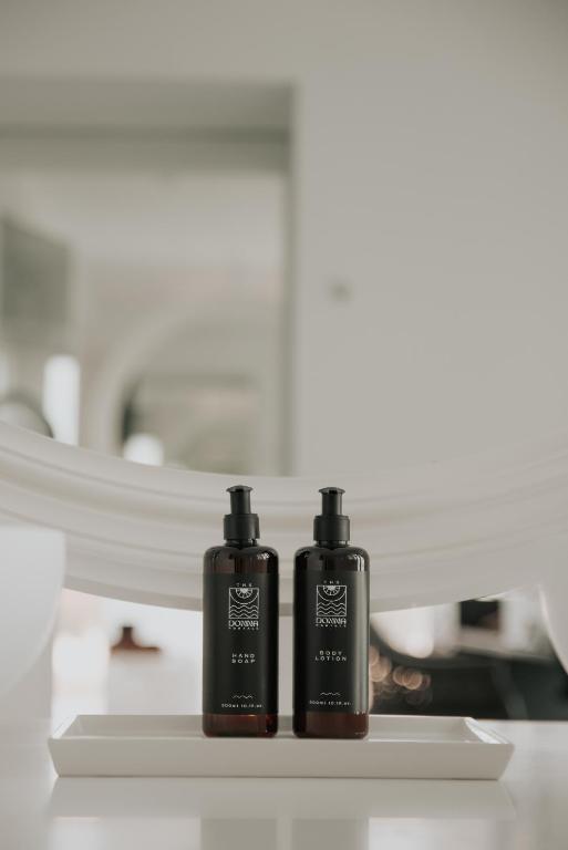 Melnas pudelēs esošs ķermeņa losjons un šampūns, izkārtoti uz baltas plāksnes mūsdienīgā interjerā.