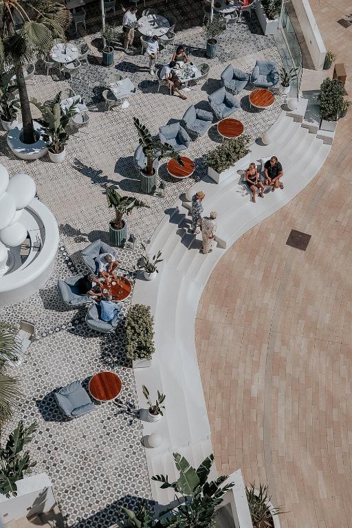 Mūsdienīga terase ar ērtām sēdvietām, augiem un cilvēkiem, kas bauda atpūtu. Gaisīga atmosfēra piedāvā lielisku vidi socializēšanai un relaksācijai.