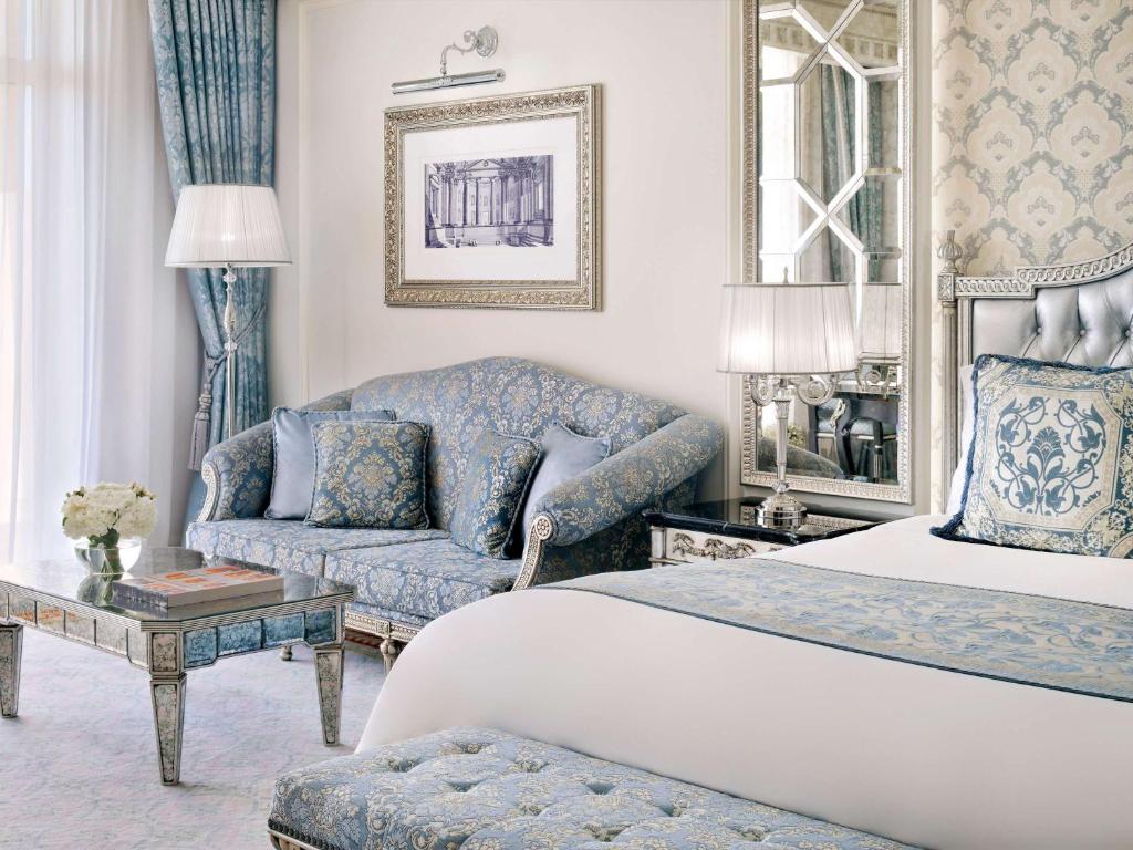 Elegants viesnīcas numurs ar zilu un sudraba interjeru, ietverot dīvānu, gultu un spoguli, radot greznu atmosfēru.