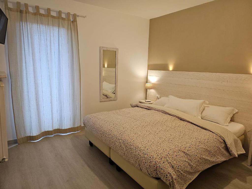 Mūsdienīga guļamistaba ar lielu gultu un dabīgu apgaismojumu, kurā ir logi ar gaišām aizkariem un elegants spogulis. Interjers ir vienkāršs un komfortabls, radot mājīgu atmosfēru.