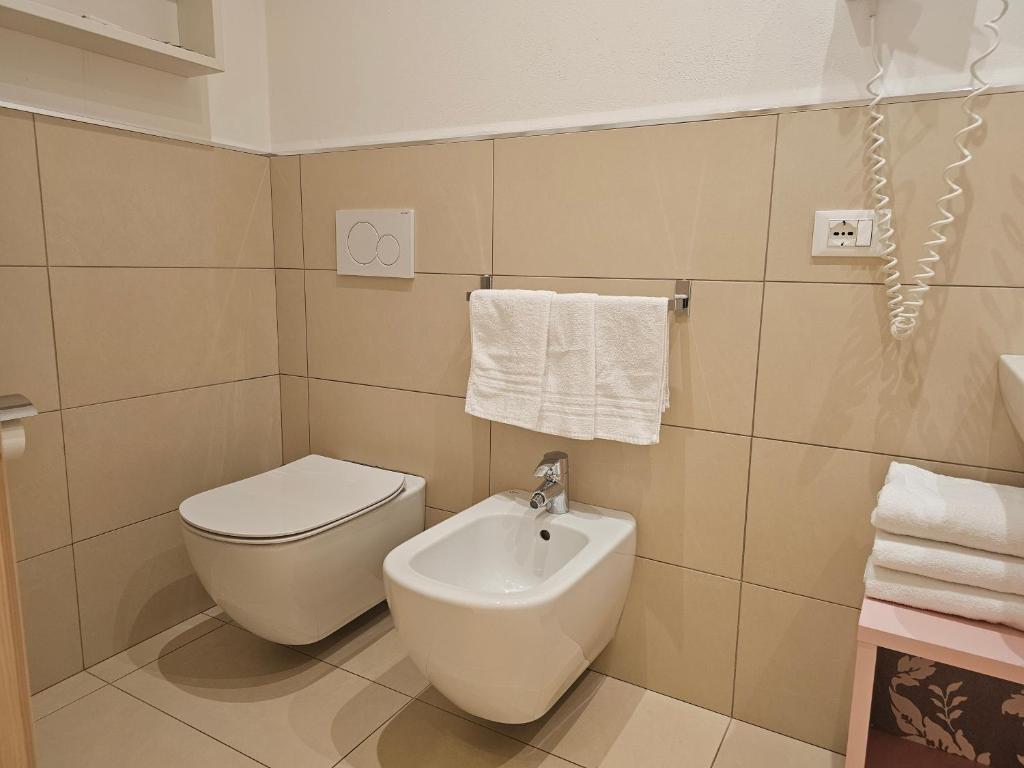 Mūsdienīgs vannas istabas interjers ar tualeti, bidē un tīrām dvieļiem. Sienas ir klātas ar gaišām flīzēm, radot elegantu un tīru izskatu.