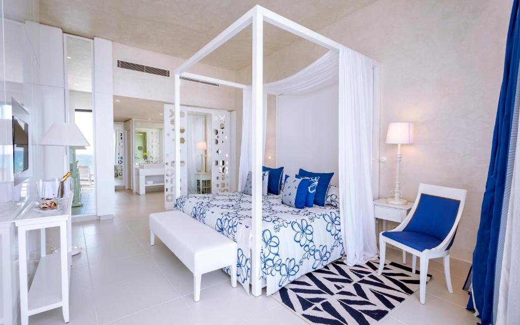 Mūsdienīga guļamistaba ar baltu četru stūru gultu, ziedu rakstu veļu un zilu akcentu. Telpa ir gaiša un plaša, ar mūsdienīgu interjeru un skatu uz dabu.