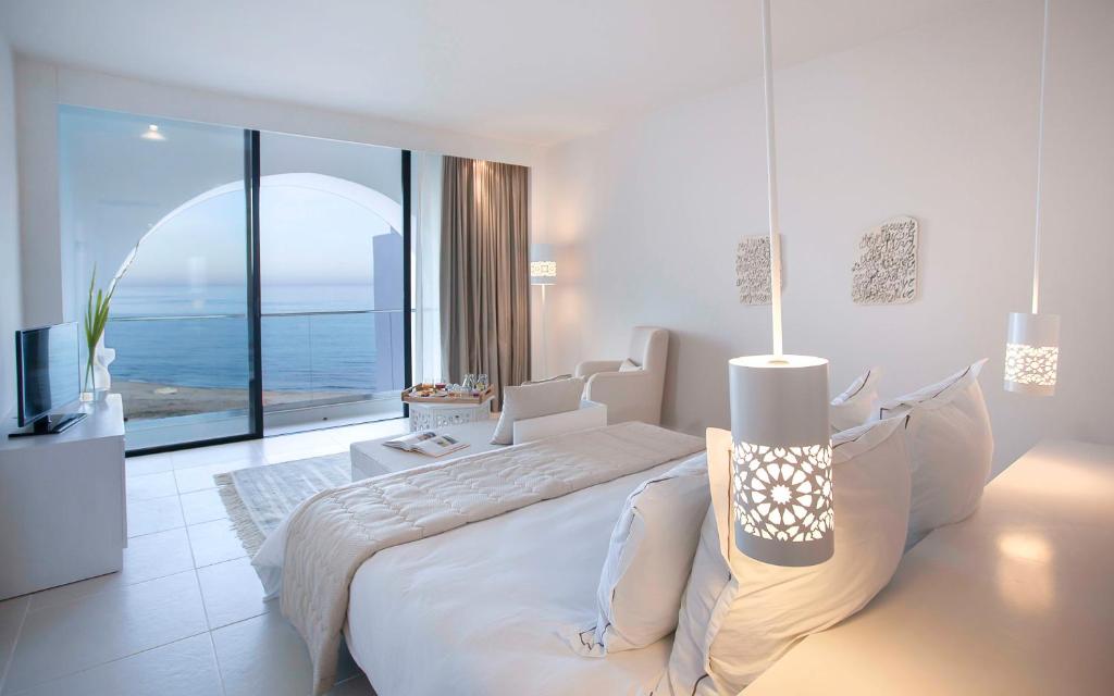 Mūsdienīga guļamistaba ar jūras skatu, gaišiem toņiem un elegantu interjeru, kas ietver stilīgas gaismas un ērti mēbeles. Ideāla vieta atpūtai un relaksācijai.
