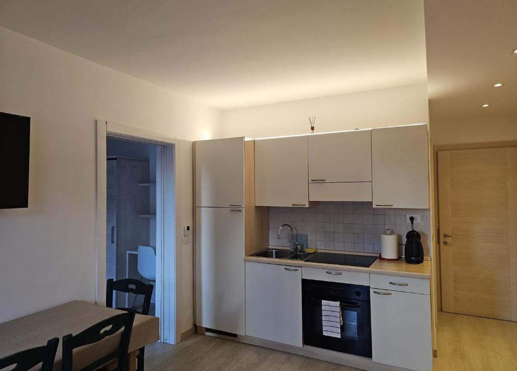 Mūsdienīga virtuve ar gaišiem skapjiem, melnu plīti un galdu ēšanai, kas rada mājīgu atmosfēru. Redzams arī televizors un durvis uz blakus telpu.