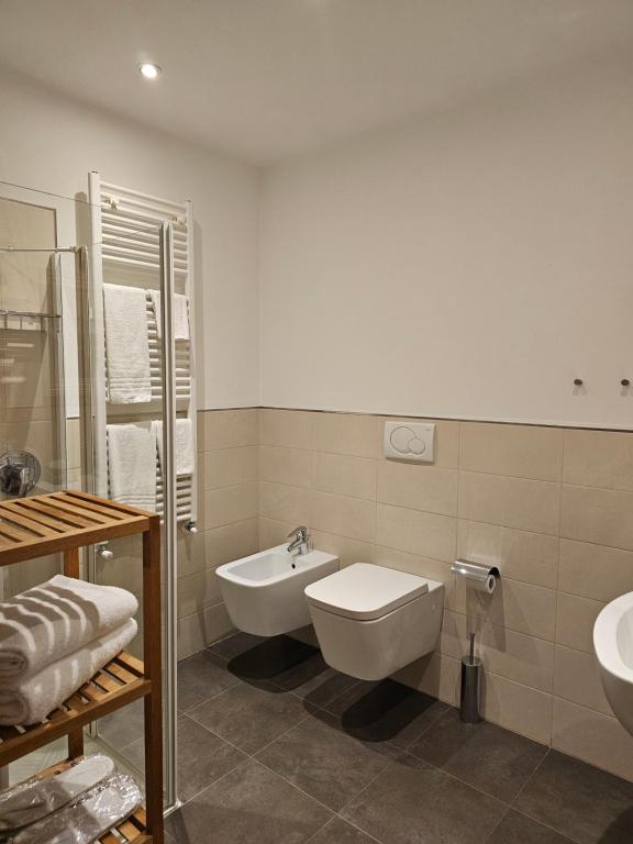 Mūsdienīgs vannas istabas interjers ar stikla dušas kabīni, baltiem dvieļiem un koka plauktu. Eleganta un funkcionāla telpa ar minimālistisku dizainu.