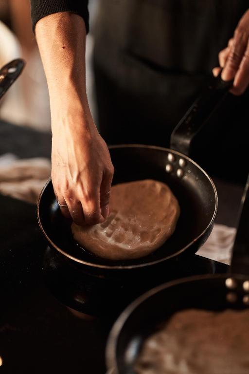 Sagatavoja mīklu pannā, izveidojot tradicionālu ēdienu. Roka ar mīklu ir redzama, pievēršoties kulinārijas procesam.