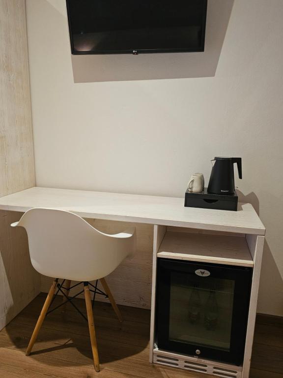Mūsdienīgs galdiņš ar baltu krēslu, televizoru pie sienas un ūdens vārītāju blakus mini ledusskapim.