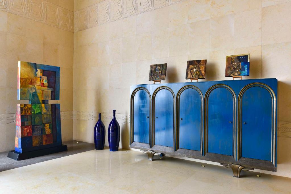 Moderns interjers ar spilgtiem mākslas darbiem, ieskaitot krāsainu statuju un stilīgu zilu skapīti ar gleznām virs tā. Eleganta atmosfēra un estētiska dizaina elementi.