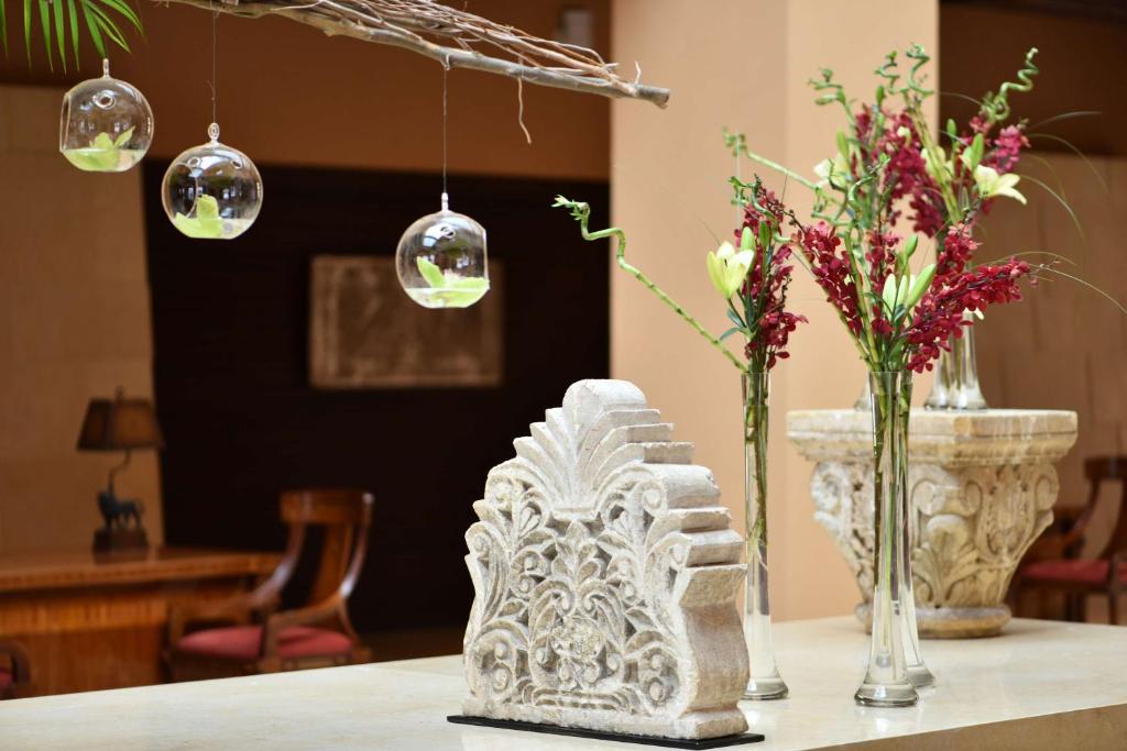 Dekoratīvs akmens elements ar greznu rakstu un ziedu kompozīcijas, kas izrotā interjeru, papildināts ar piekārtiem stikla globusiem ar lapām.