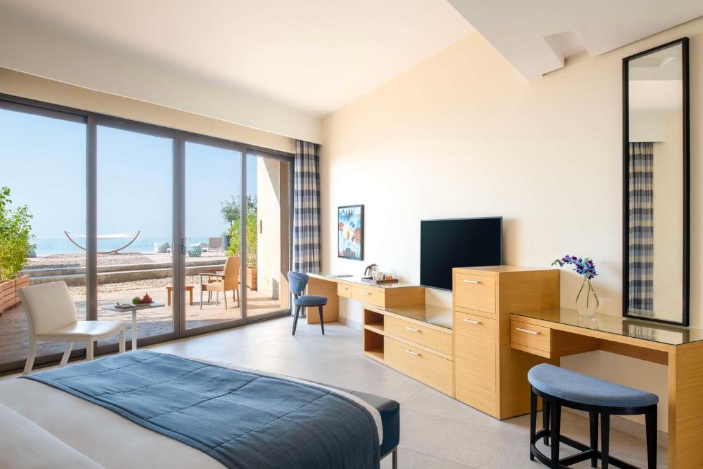 Mūsdienīgs viesnīcas numurs ar plašu skatu uz jūru, kurā ir ērti mēbelēta zona, televizors un darba galds. Lielas stikla durvis ved uz terasi ar atpūtas zonu.