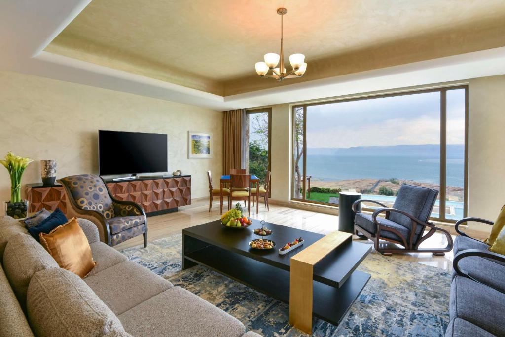 Mūsdienīgs viesistabas interjers ar plašu skatu uz jūru, iekārtots ar ērtiem dīvāniem, TV un elegantu galdu. Gaismas un dabiskā apgaismojuma bagāta telpa rada mājīgu atmosfēru.