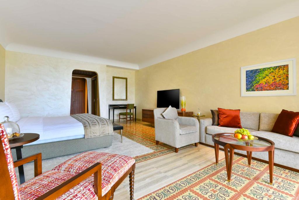 Moderns viesnīcas numurs ar ērtu dīvānu, galdu un TV, kā arī dekoratīvām gleznām un augļu šķīvi. Interjers ir gaišs un elegants.