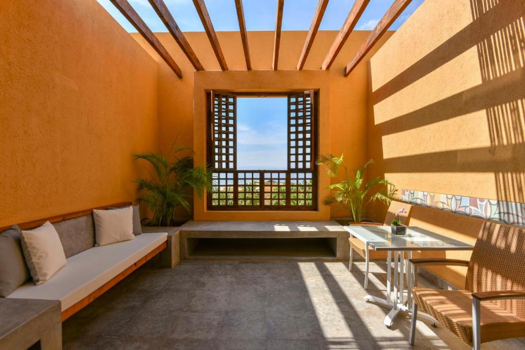 Gaiša un moderna atpūtas telpa ar oranžiem sienām, koka sijām un skatu uz dabu. Telpā ir ērta dīvāna zona un galds ar krēslu.