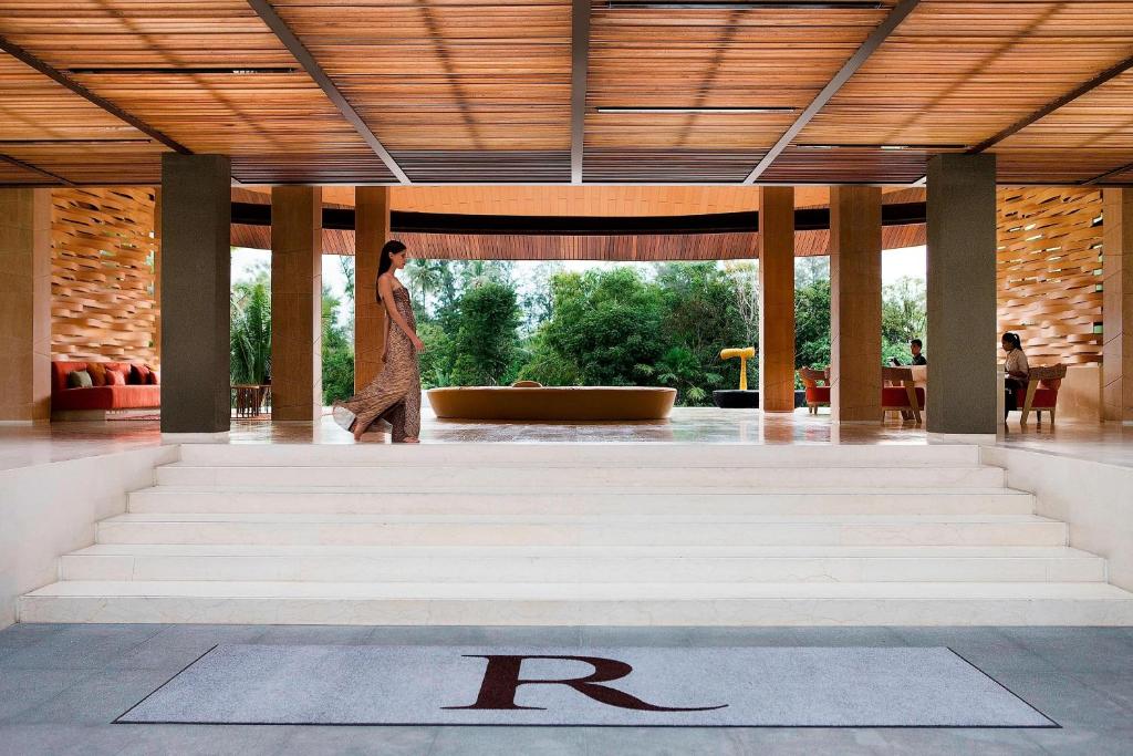 Elegants interjers viesnīcas vestibilā ar modernu dizainu un dabas ainavu fonā, kur sieviete staigā pa kāpnēm.