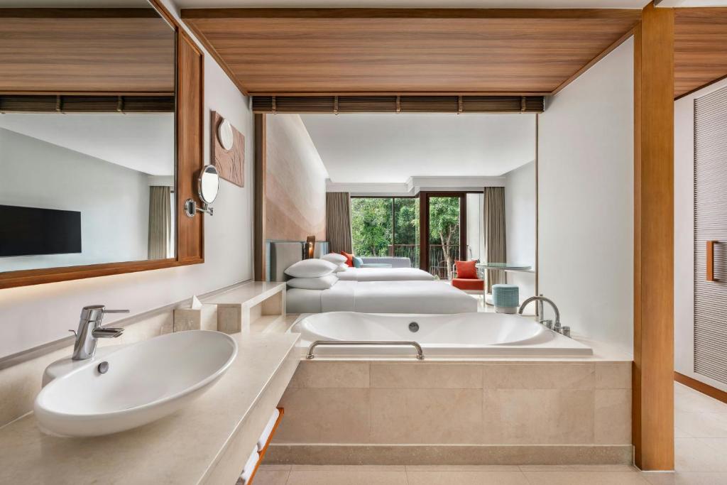 Mūsdienīgs vannas istabas interjers ar koka akcentiem un lielu spoguli, kas atspoguļo viesnīcas numuru ar dabu. Vannā ir eleganta dizaina izskats un harmoniska krāsu palete.