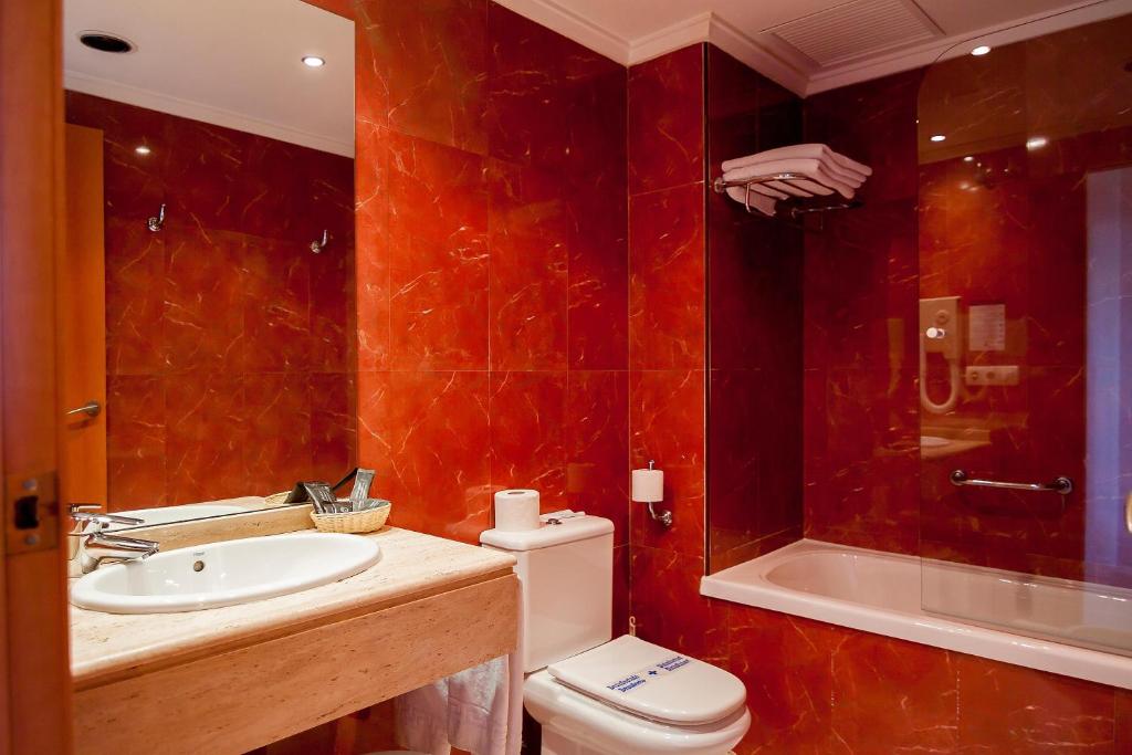 Mūsdienīgs vannas istabas interjers ar sarkanu akmens apdari, kas ietver vannu, tualeti un izlietni. Eleganta dizaina elementi un labi organizēts telpas plānojums.