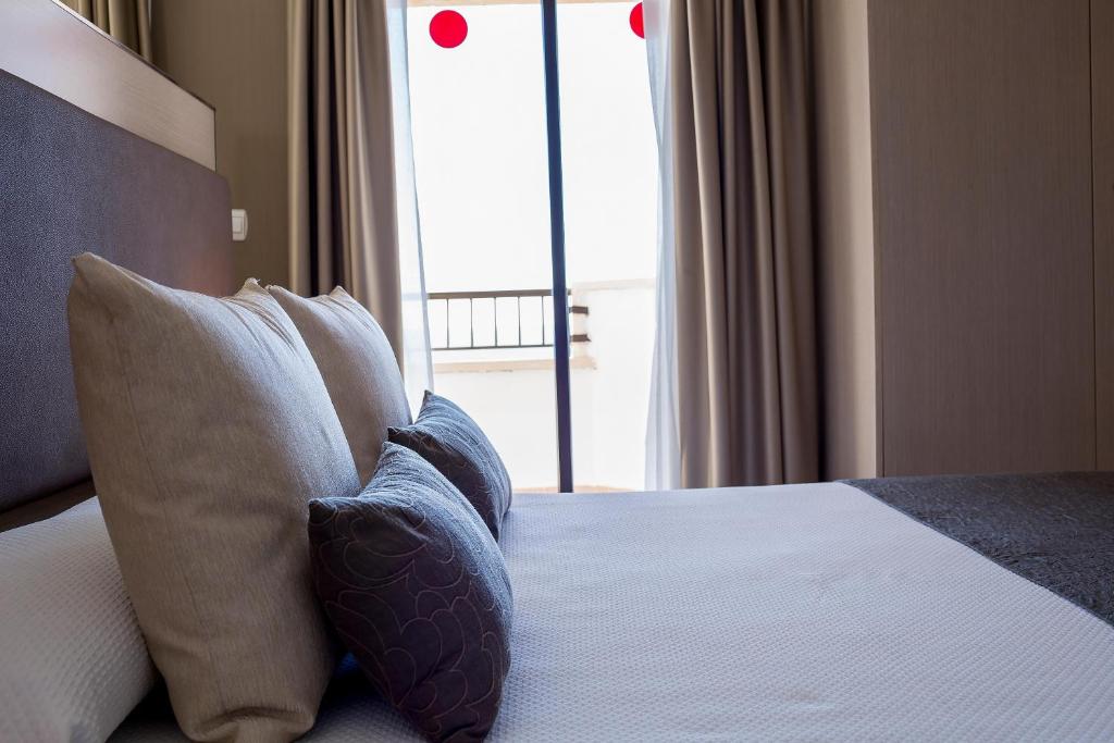 Mūsdienīgs guļamistabas interjers ar ērtām spilveniem un skatu uz balkonu. Gaisīgas aizkari un gaiša krāsa piešķir telpai komforta sajūtu.