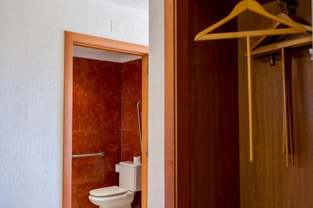 Mūsdienīgs vannas istabas skats ar siltu toņu flīzēm un koka skapja elementiem. Redzams tualetes pods un dušas stūris.