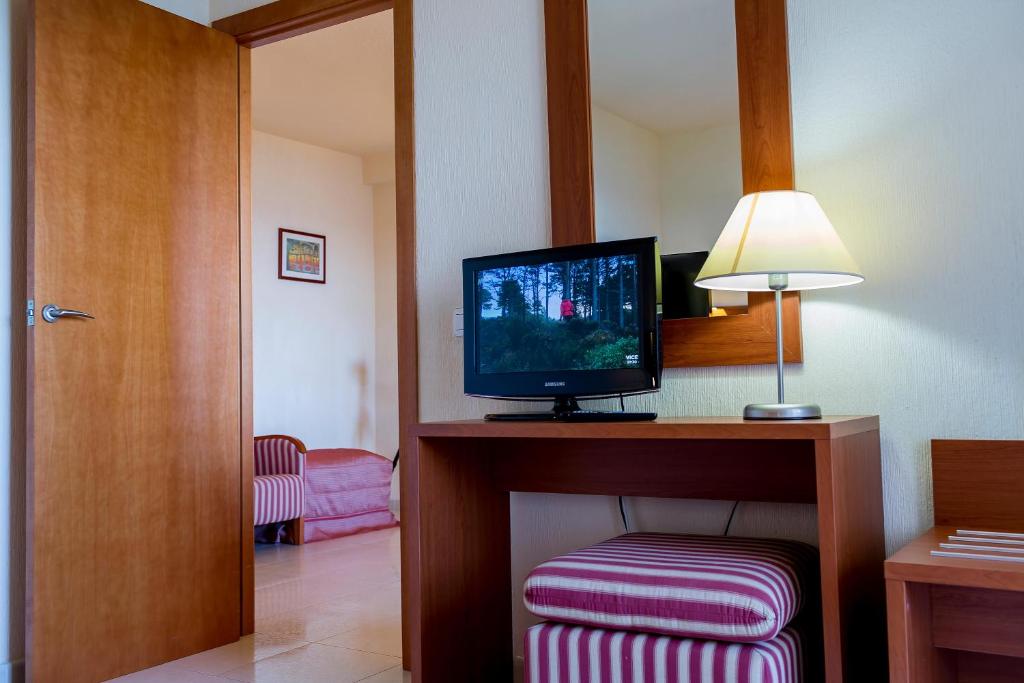 Mūsdienīgs viesnīcas numurs ar koka mēbelēm, televizoru un lampu, redzama durvju ejas daļa.