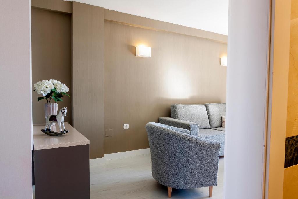 Mūsdienīgs viesnīcas numurs ar pelēku dīvānu un krēslu, dekorēts ar ziediem un nelielu dekoratīvu figūru. Sienas ir gaišas un siltas, radot mājīgu atmosfēru.