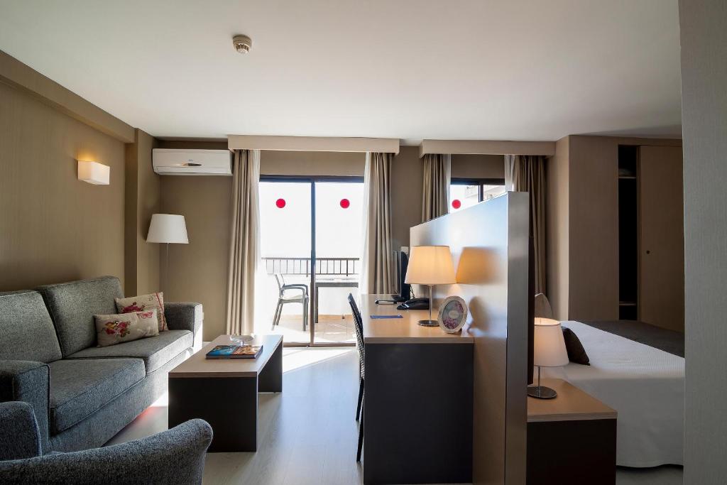 Mūsdienīgs viesnīcas numurs ar atsevišķu dzīvojamo zonu, dīvānu un darba galdu, kas piedāvā dabisko apgaismojumu un piekļuvi balkona durvīm.