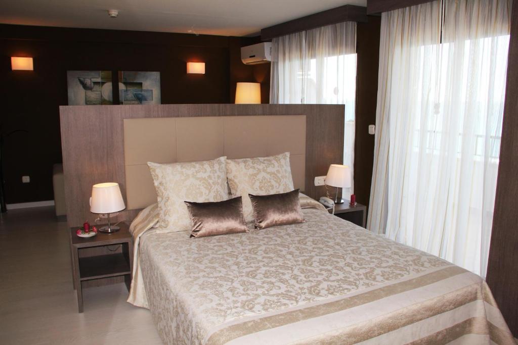 Mūsdienīga guļamistaba ar stilīgu gultu un elegantiem spilveniem, papildināta ar mīksto apgaismojumu un plānām aizkariem, kas rada mājīgu atmosfēru.