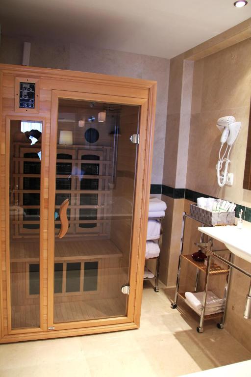 Sauna ar stikla durvīm modernā vannas istabā, ap to izvietoti dvieļi un higiēnas piederumi. Ideāla vieta relaksācijai un labsajūtai.