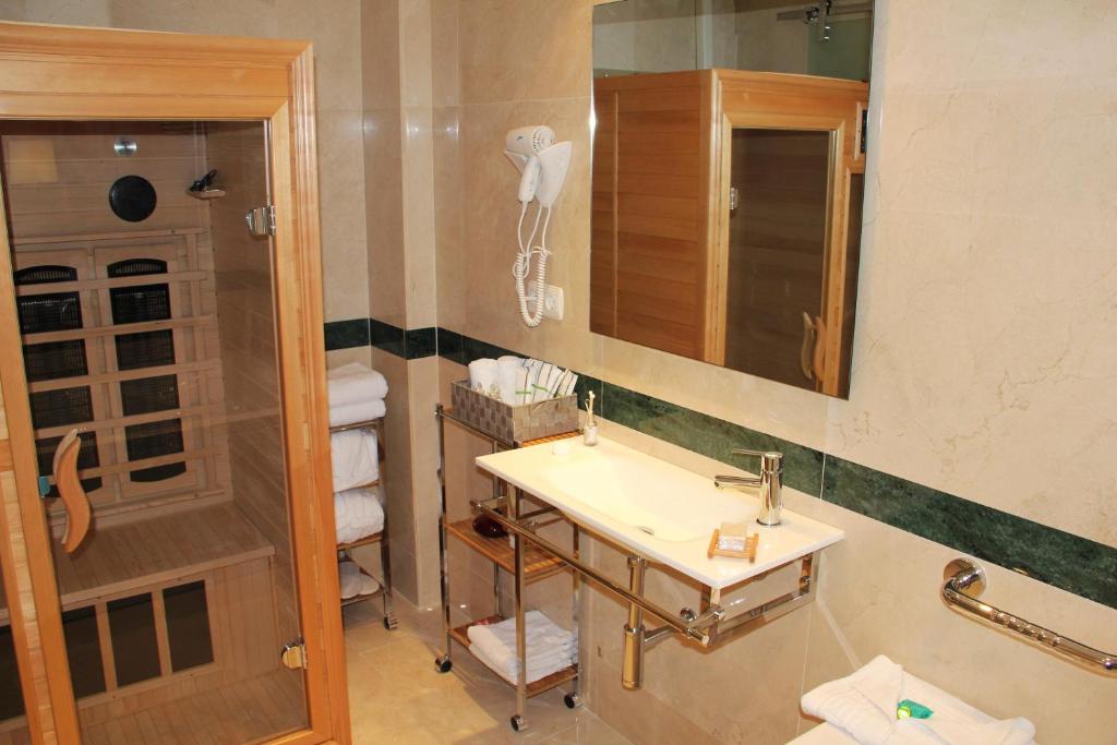 Mūsdienīga vannas istaba ar saunu, elegantu izskatu un stikla durvīm. Uz izlietnes ir dažādi higiēnas piederumi un dvieļi, kas pieejami uz plaukta.