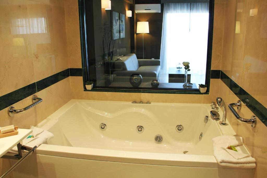 Luksusa vannas istaba ar hidromasāžas vannu un skatu uz viesistabu, kas ir eleganti iekārtota ar mīksto dīvānu un gaismas avotiem.