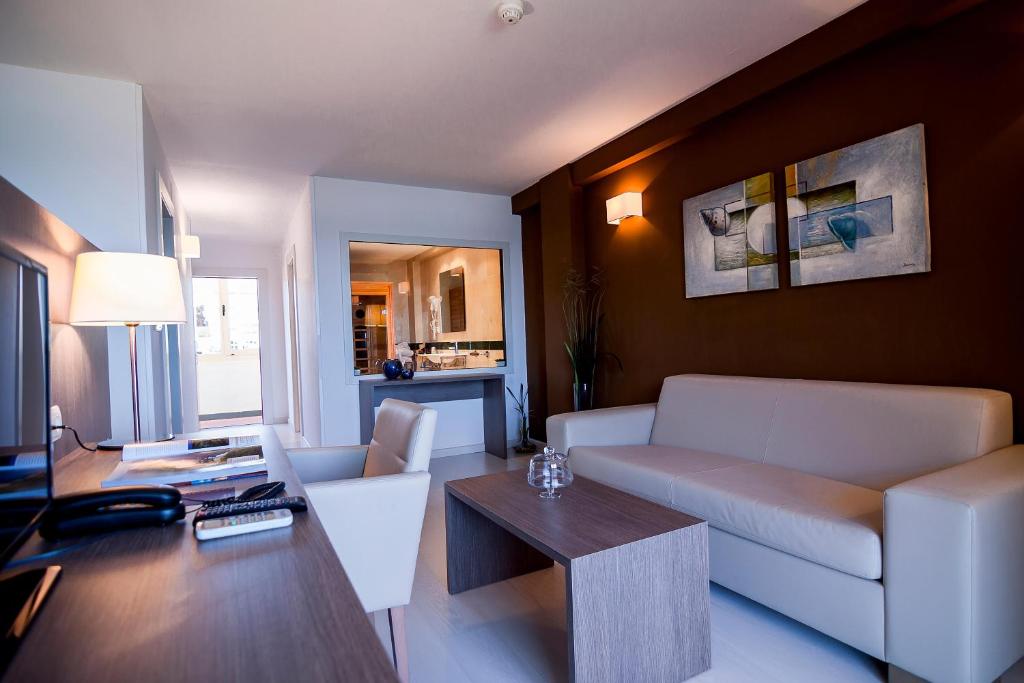 Mūsdienīga viesnīcas istaba ar gaisīgu interjeru, ērtiem dīvāniem un mākslas darbiem uz sienām. Redzama arī virtuve un darba zona.