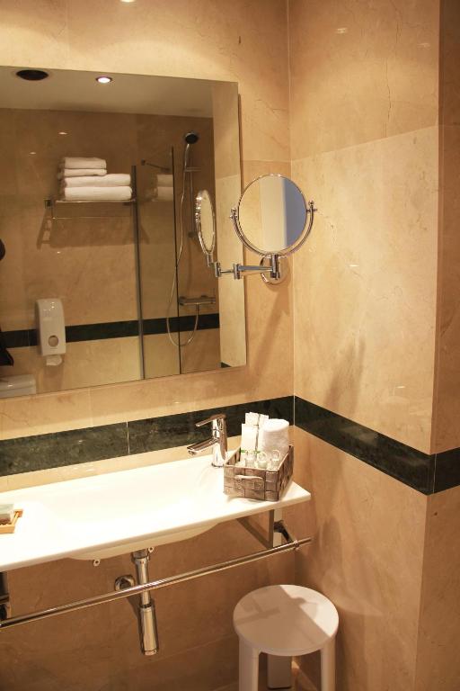 Elegants un moderns vannas istabas interjers ar marmora apdari, spoguli un higiēniskajiem piederumiem. Uz galda redzami dvieļi un higiēnas līdzekļi.