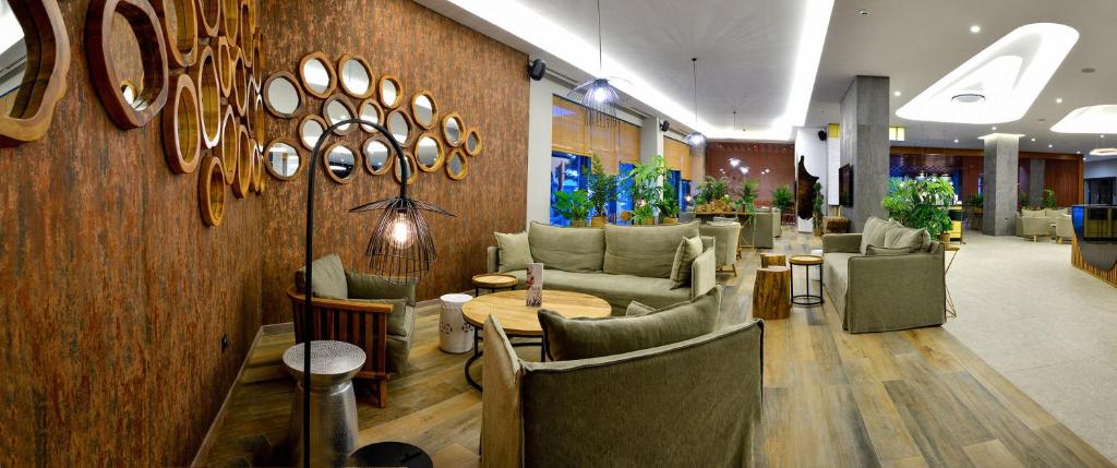 Mūsdienīga viesnīcas uzgaidāmā telpa ar komfortablām mēbelēm, stilu veidojošām spoguļu elementiem un daudz zaļumu, radot relaksējošu atmosfēru.