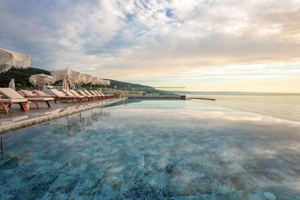 Luksusīga pludmales baseina zona ar sauļošanās krēsliem un skatu uz jūru, kas nodrošina mierīgu un relaksējošu atmosfēru. Ideāla vieta atpūtai un izklaidei.