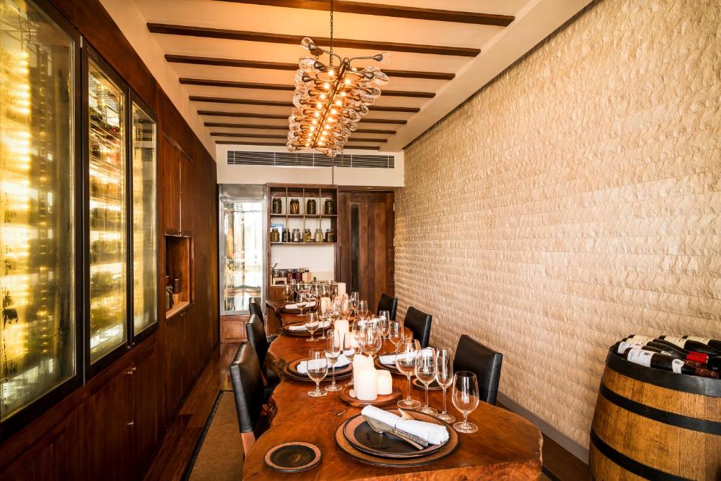 Mūsdienīgs restorāna iekšskats ar elegantu galdu, kas klāts ar glāzēm un dekoriem, un vīna glabātuvi fonā. Interjers apvieno koka elementus un modernu apgaismojumu.