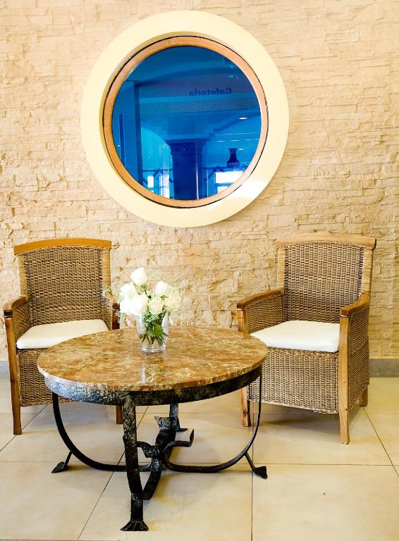 Mūsdienīgs interjers ar divām vītņu krēslām un marmora galdu, papildināts ar pušķi baltām rozēm. Apaļa loga forma rada gaisīgu noskaņu un pievieno estētiku telpai.