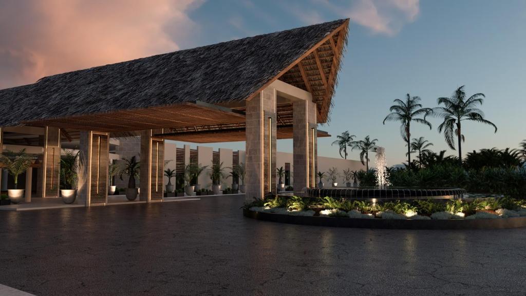 Mūsdienīga viesnīcas ieeja ar jumtu, kas izgatavots no dabīgām materiālām, apkārt esošām palmām un dārzu elementiem, kā arī strūklaku, kas rada relaksējošu atmosfēru.