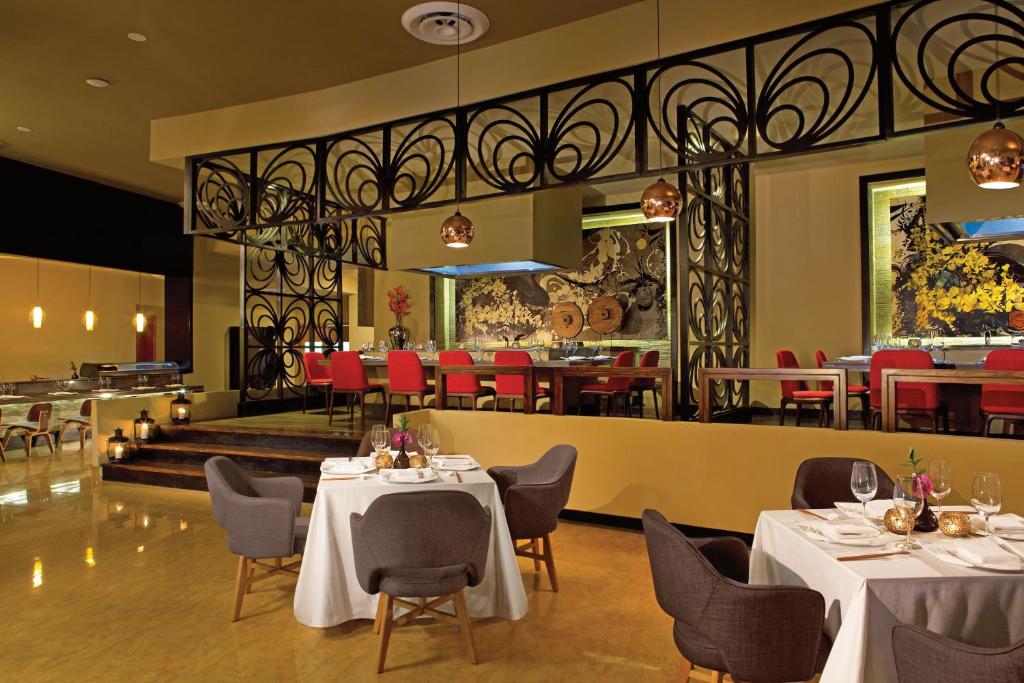 Mūsdienīgs restorāns ar elegantiem galdiem un krēsliem, dekorēts ar mākslinieciskām detaļām un siltu apgaismojumu. Interjerā ir redzama stilīga metāla struktūra un krāsaini mākslas darbi.