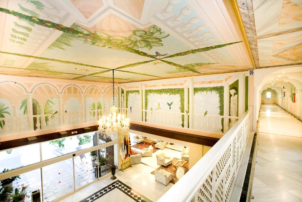 Elegants viesnīcas vestibuls ar greznu griestu gleznojumu un dekoratīvām sienām, kas rotā zaļumi un putni. Interjers ir gaišs un plašs, radot viesmīlīgu atmosfēru.