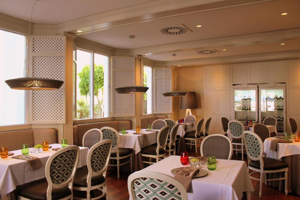 Elegants restorāns ar gaišiem interjera toņiem un elegantiem galdiem, kas rotāti ar krāsainām glāzēm. Lielie logi nodrošina dabisko apgaismojumu un skatu uz dārzu.