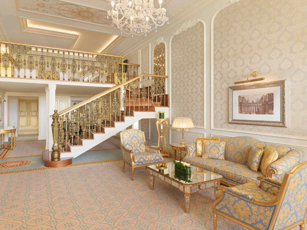 Greznas viesistabas interjers ar elegantu kāpņu konstrukciju, zeltītām detaļām un stilīgiem mēbeļu komplektiem. Apgaismojums un dekorācijas piešķir telpai greznu atmosfēru.