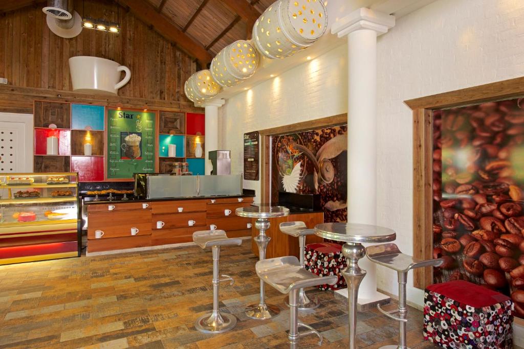 Kafijas veikala iekšskats ar modernu interjeru, koka un metāla elementiem, un krāsainām sienām, kas rotā kafijas tēmu. Redzamas kafijas izstrādājumu vitrīnas un stilīgas sēdvietas.