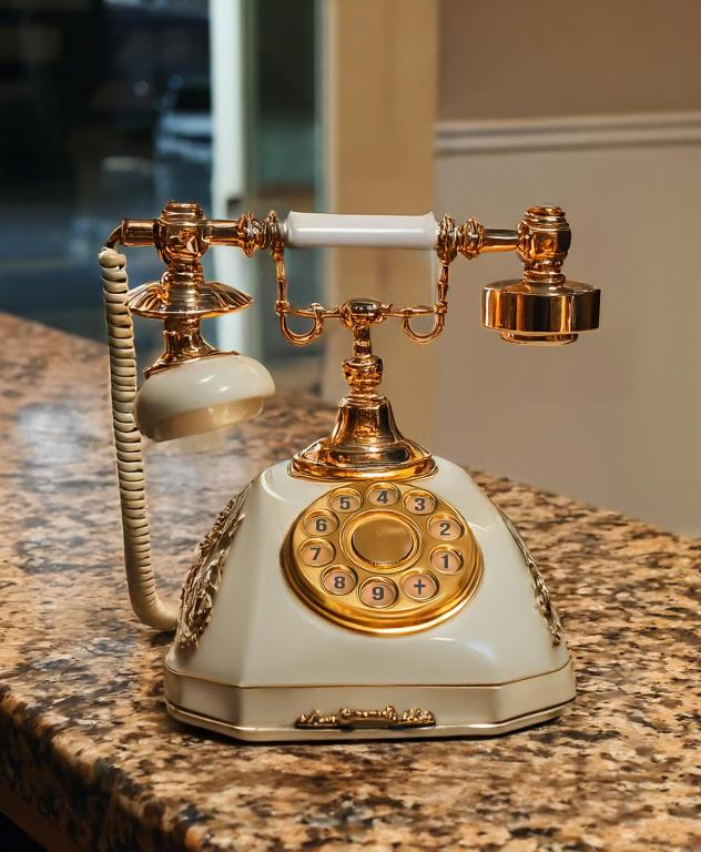 Retro stilā izstrādāts telefons ar zeltītām detaļām un rotājumiem, novietots uz granīta virsmas.