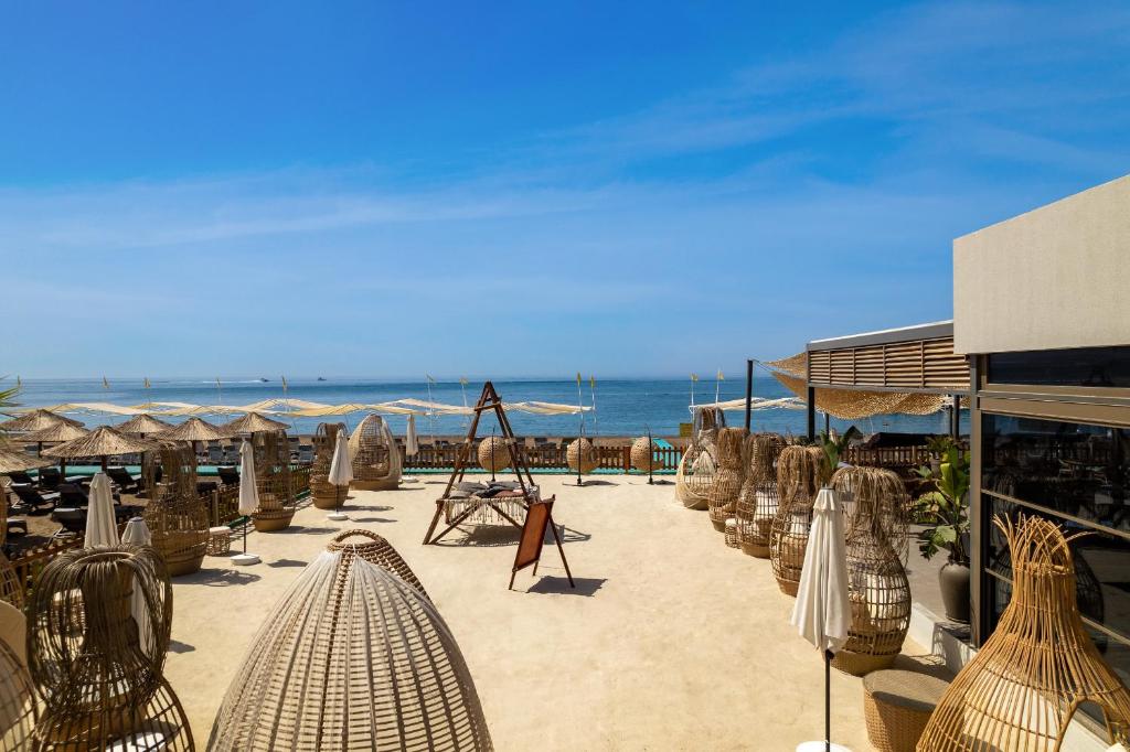 Pludmales atpūtas zona ar vītņu krēsliem un saulessargiem, skats uz jūru zem skaidra zila debesīm.